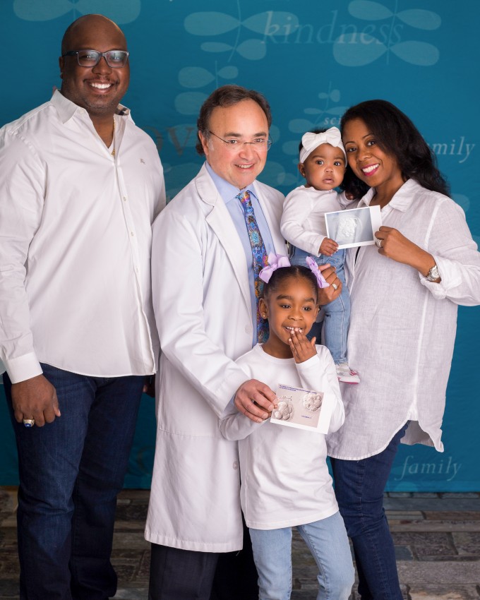 Uconn Fertility success story image of reproductive endocrinologist Claudio Benadiva posing with mother, father, young daughter and new baby. Mom holding image of embryo prior to transfer.